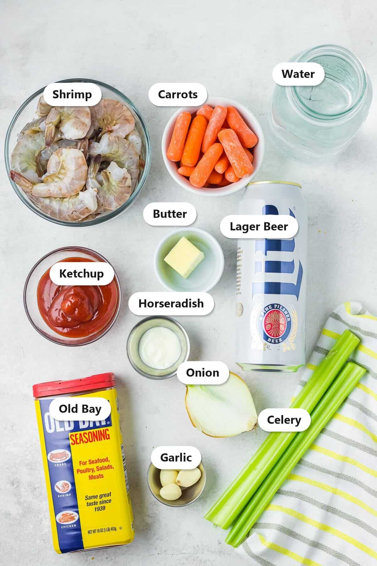 Labeled ingredients for peel and eat shrimp including raw shrimp, lager beer, Old Bay, carrots, celery, onion, garlic, and butter.