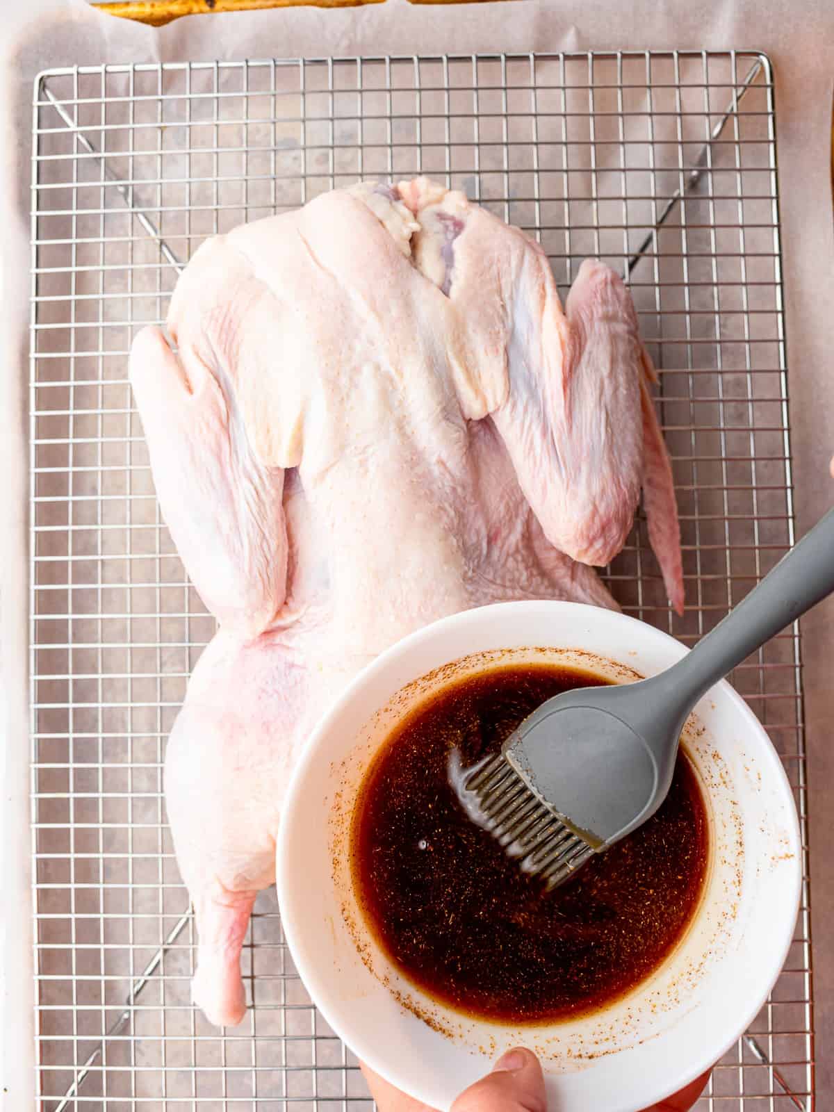 Raw whole duck set breast side up on a wire rack with five spice marinade, ready to roast for Peking duck.