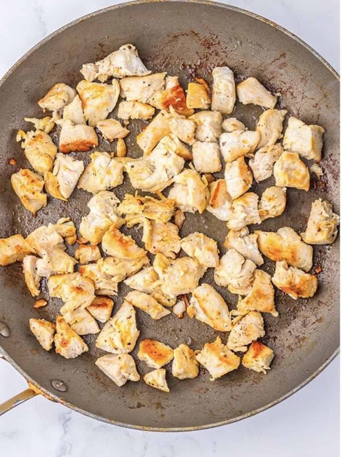 Diced chicken breast browning in butter in a skillet.