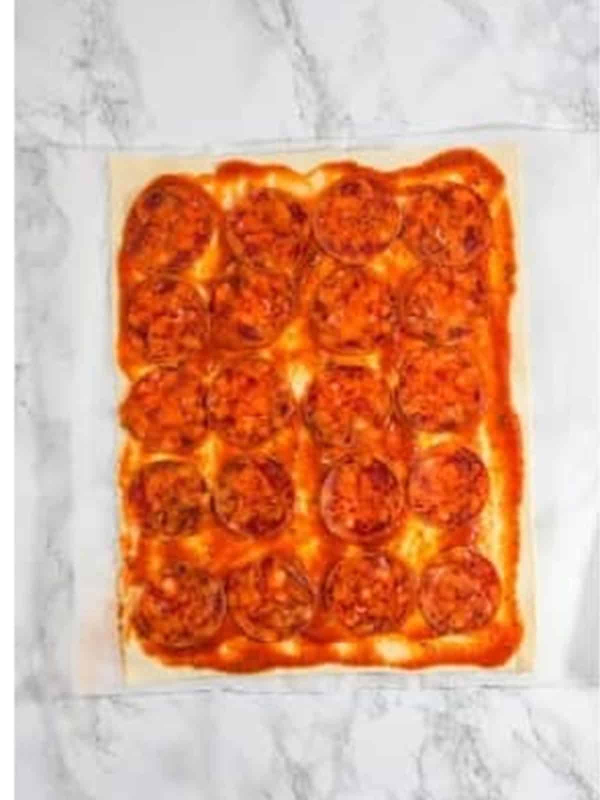 Pepperoni slices arranged evenly over the sauced puff pastry.