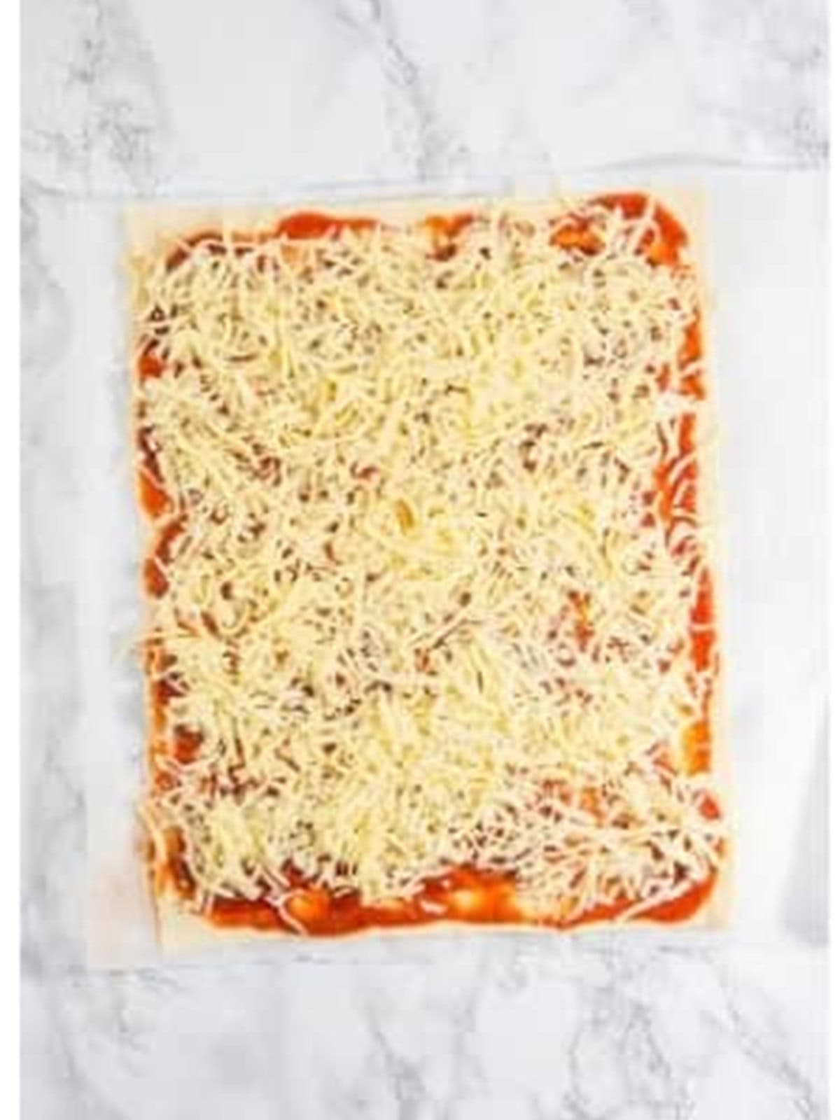 Shredded mozzarella sprinkled over the pepperoni layer for pepperoni rolls.