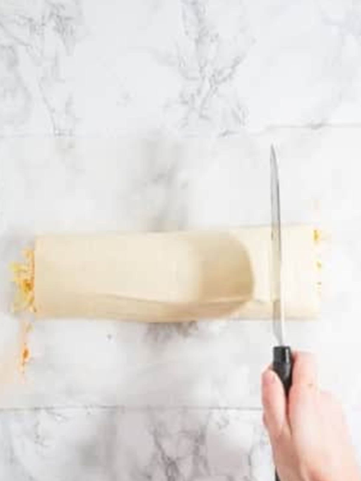 Serrated knife slicing the pepperoni roll log into even pieces.