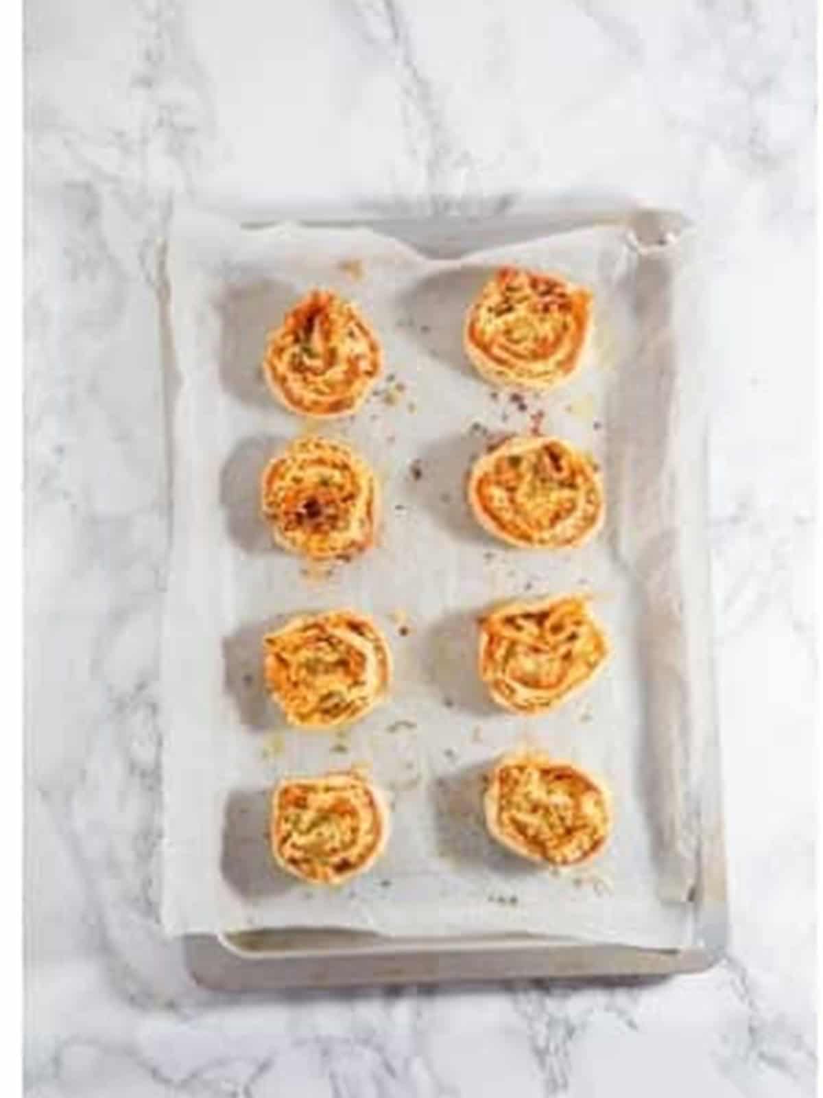 Pepperoni roll slices spaced out on a parchment lined baking tray.