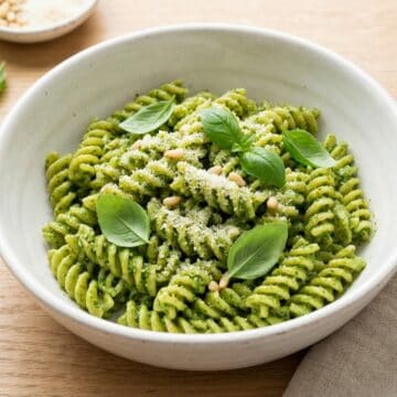 A white bowl of creamy basil pesto pasta topped with parmesan and fresh basil.
