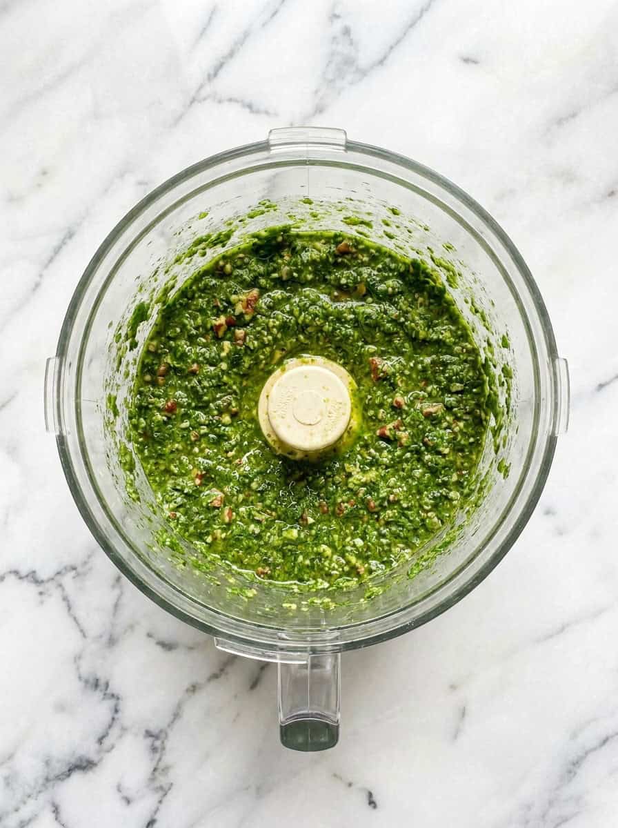 Fresh bright green basil pesto blended in a food processor bowl.