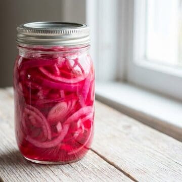A glass jar filled with bright pink pickled red onions.
