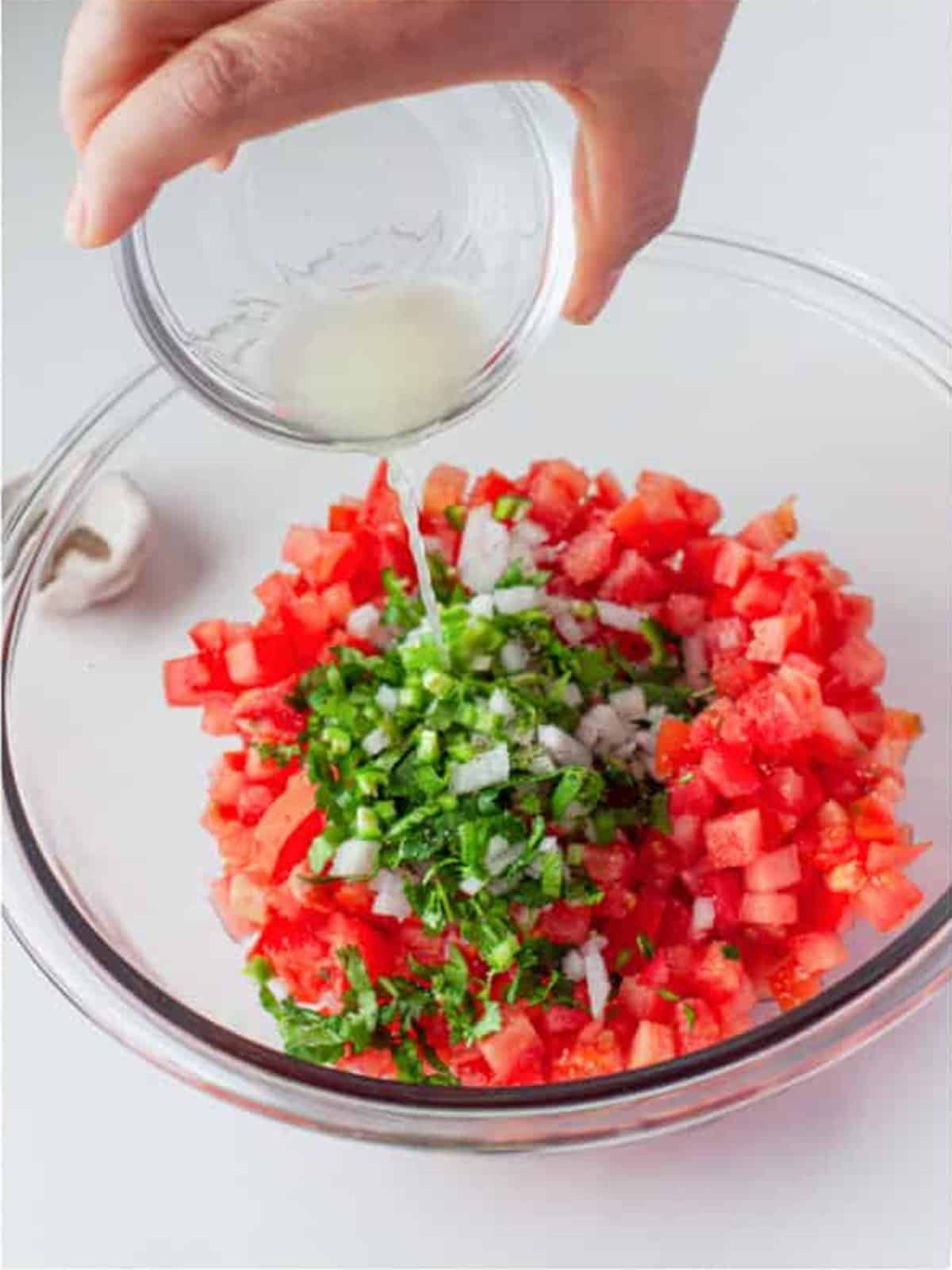 Pouring fresh lime juice over the pico de gallo mixture in a glass bowl.
