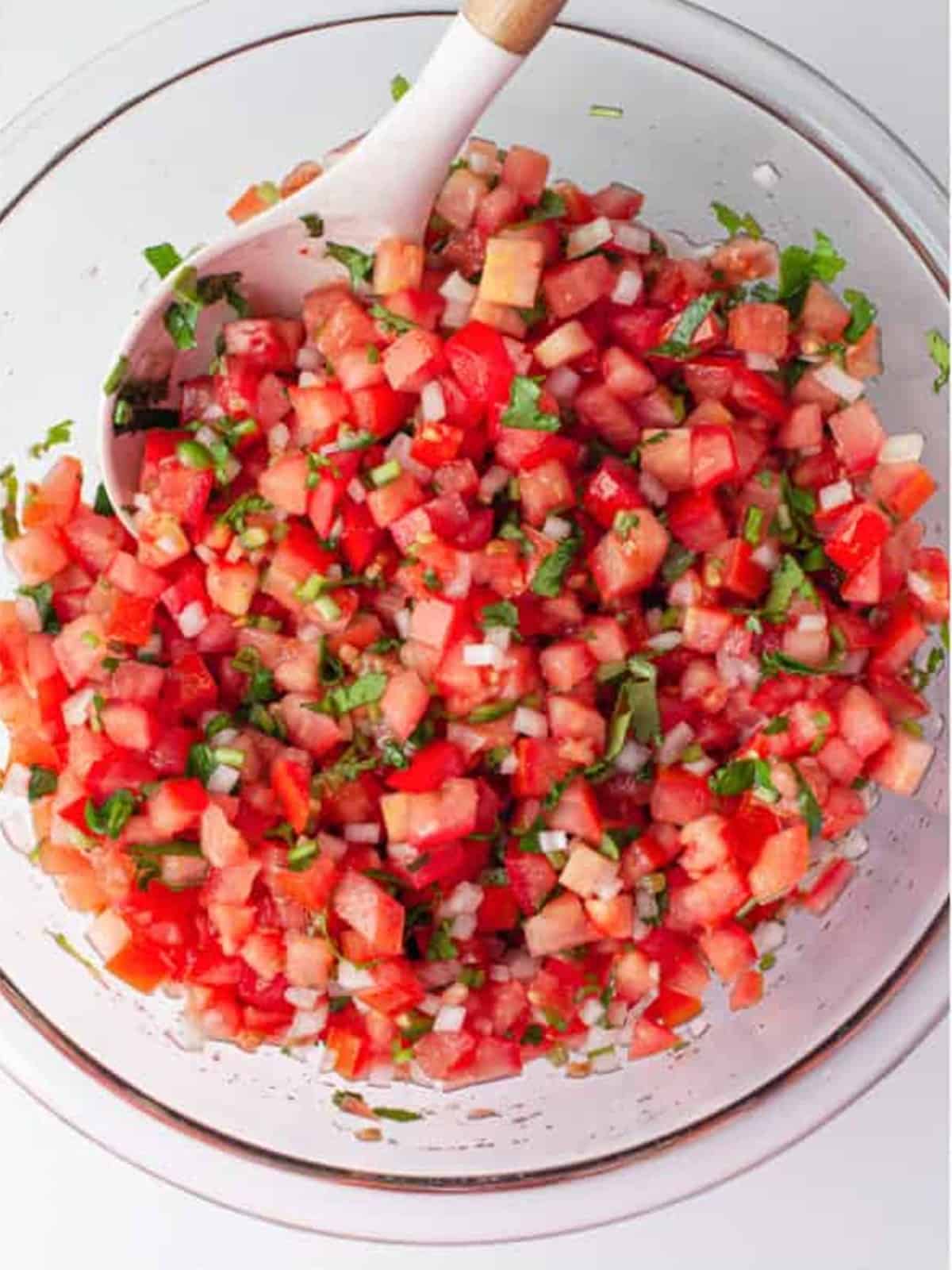 Finished pico de gallo tossed together in a glass bowl with a spoon.