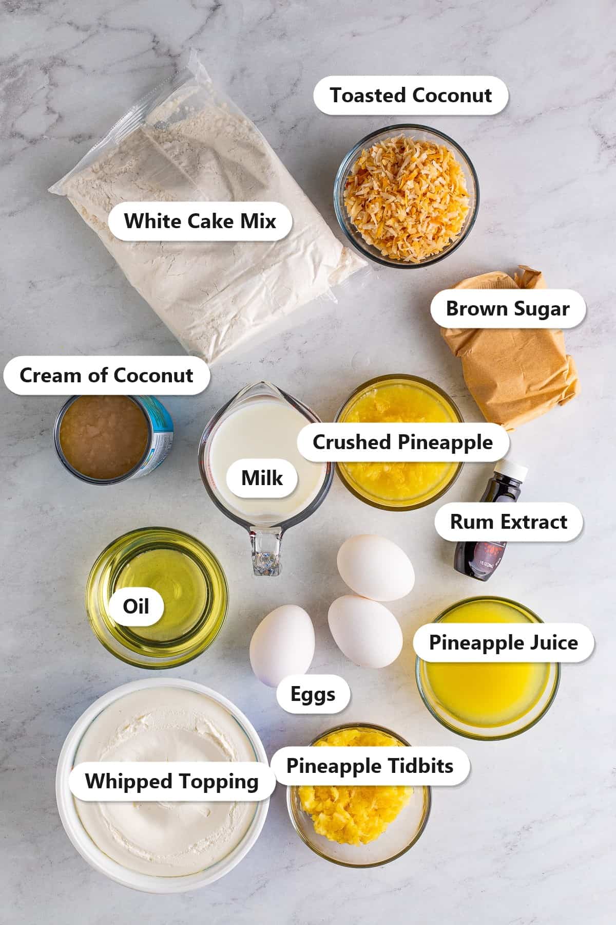 Labeled ingredients for Pina Colada Cake including white cake mix, cream of coconut, crushed pineapple, pineapple juice, toasted coconut, whipped topping, eggs, oil, milk, brown sugar, and rum extract.