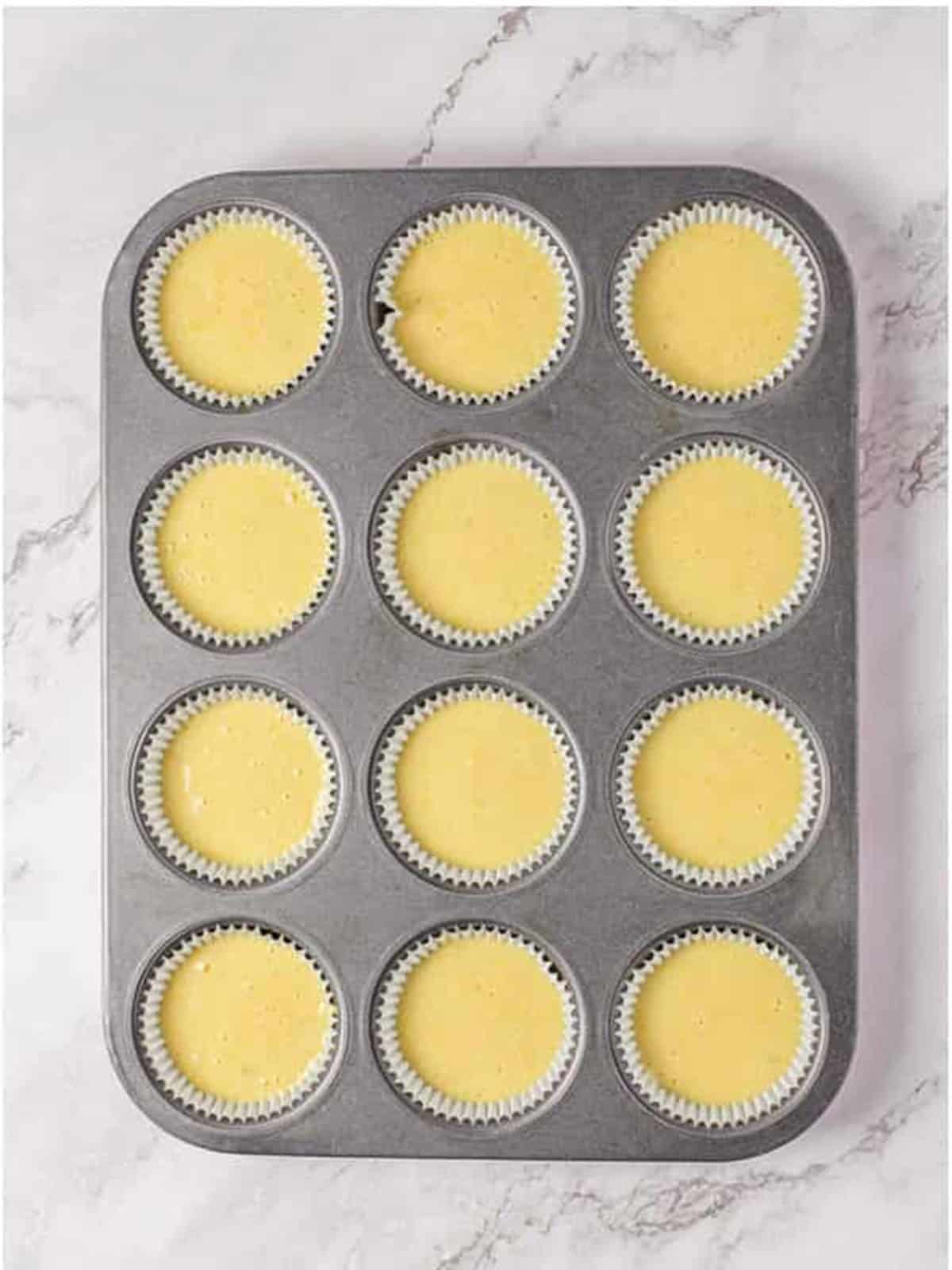 Pina colada cupcake batter divided into a lined muffin tin.