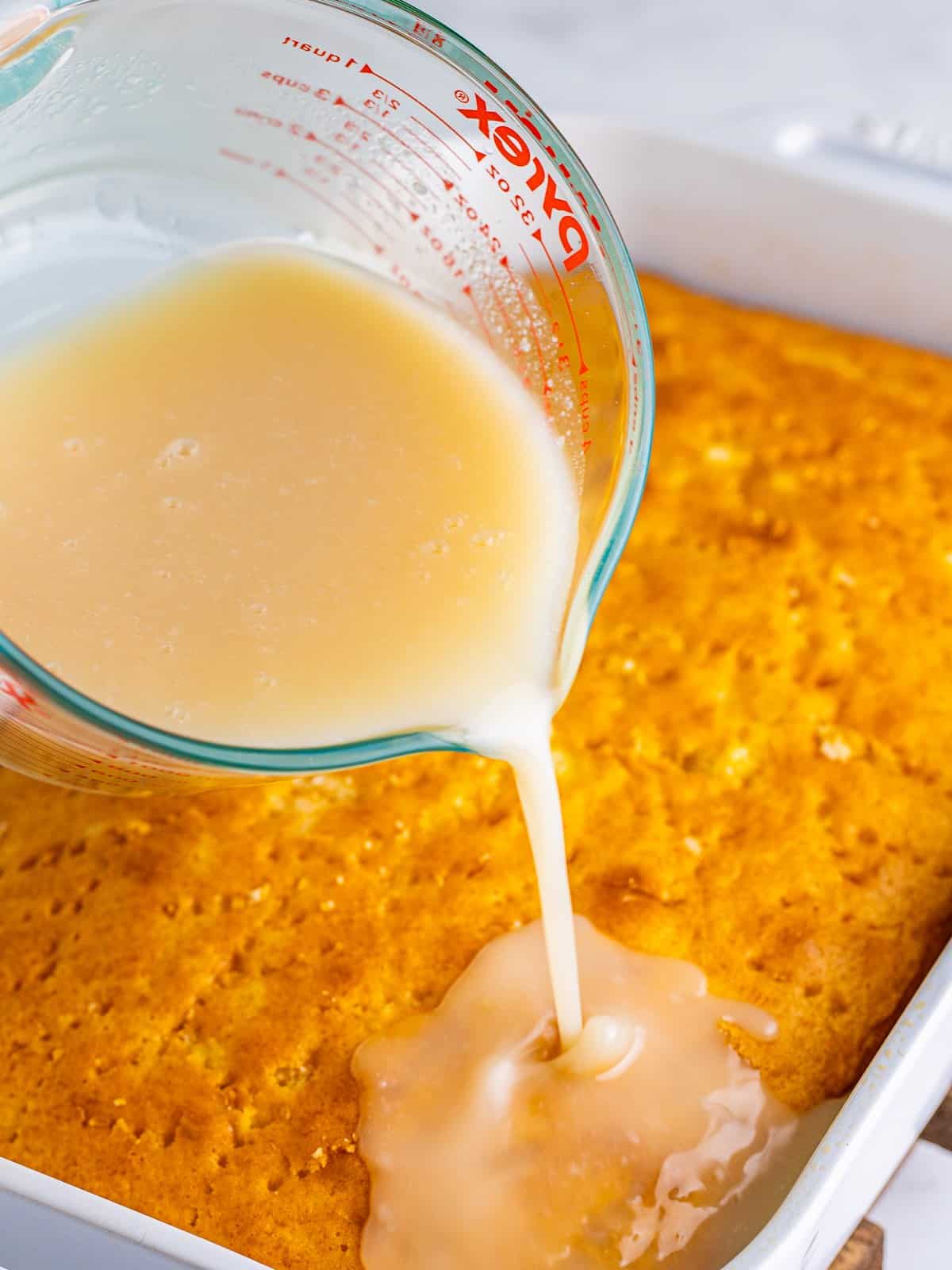 Pouring cream of coconut soak over the poked cake for Pina Colada Cake.
