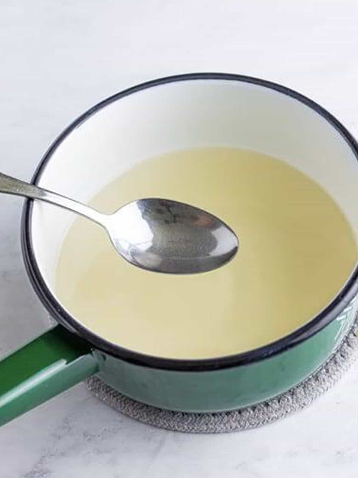 Sugar and water dissolving into simple syrup in a small saucepan for pineapple coconut lemonade.
