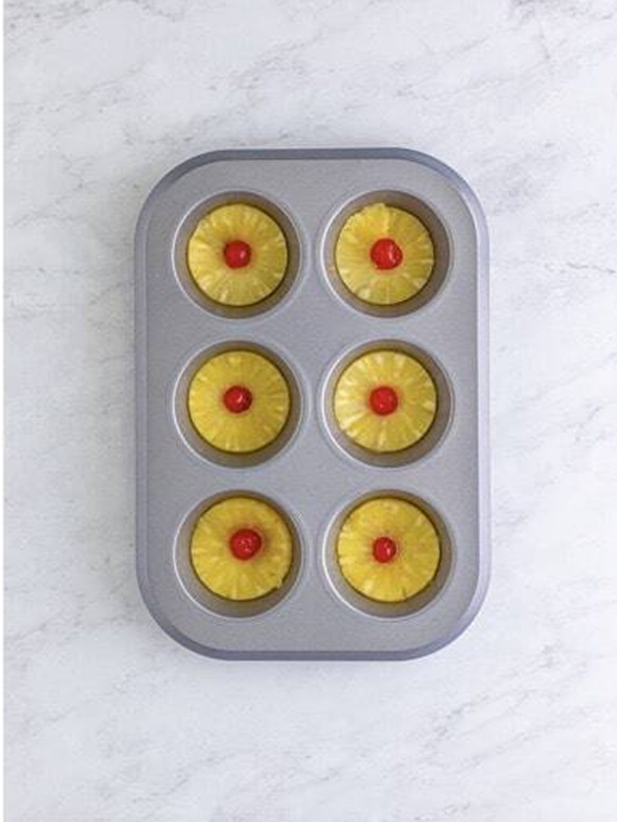 Pineapple rings and maraschino cherries placed over the sauce in a muffin tin.