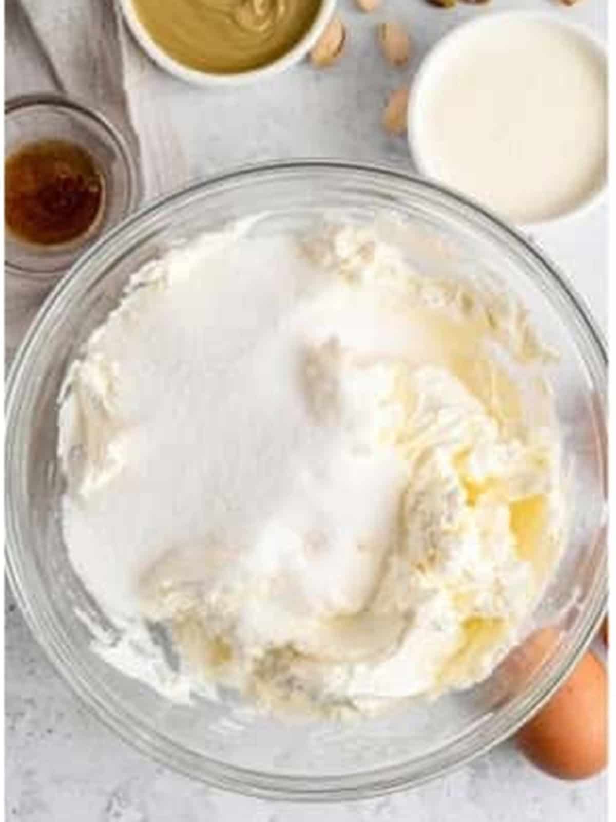 Cream cheese and sugar in a mixing bowl for pistachio cheesecake.