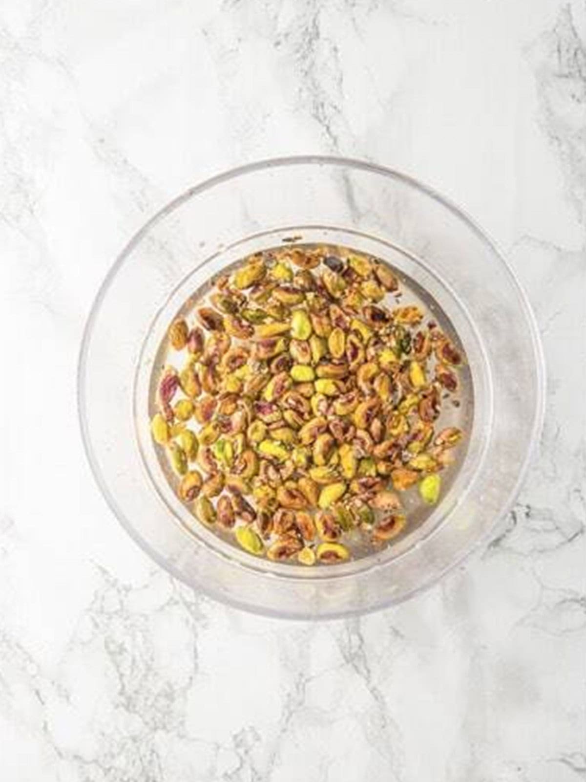 Raw pistachios soaking in a bowl of water to hydrate.