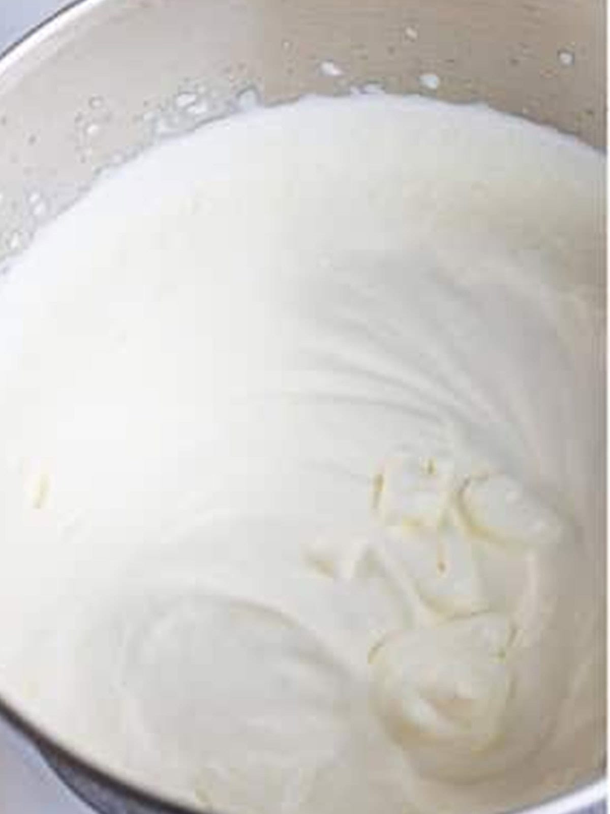 Heavy whipping cream whipped to soft peaks in a stand mixer bowl for no churn pistachio ice cream.