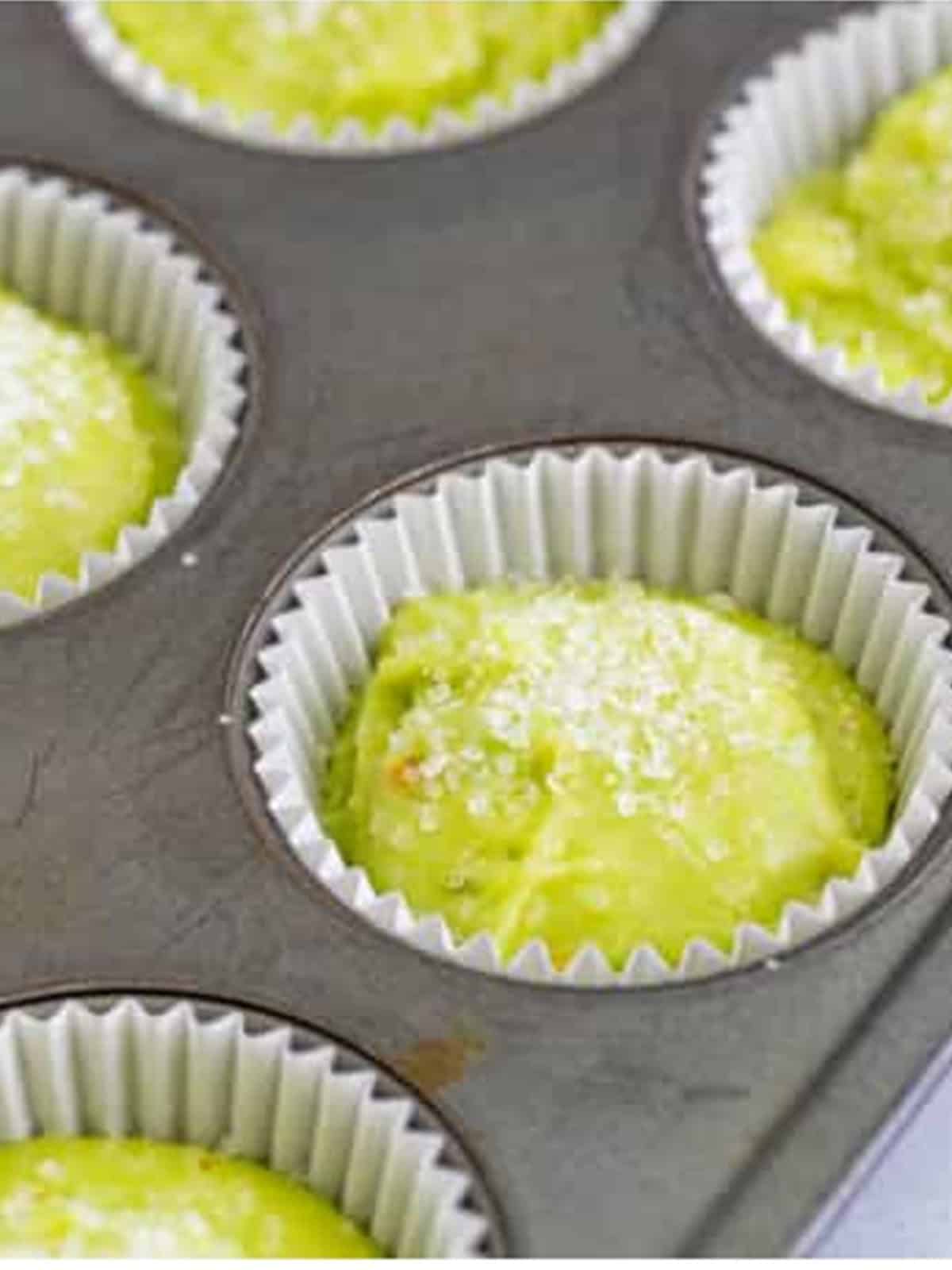 Pistachio muffin batter divided into a lined muffin tin and topped with sugar.