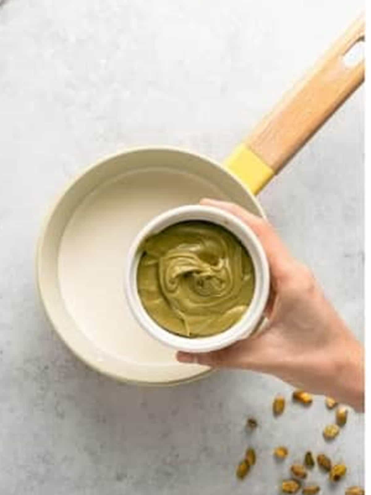 Adding pistachio spread to milk and cream in a saucepan for pistachio pudding recipe.