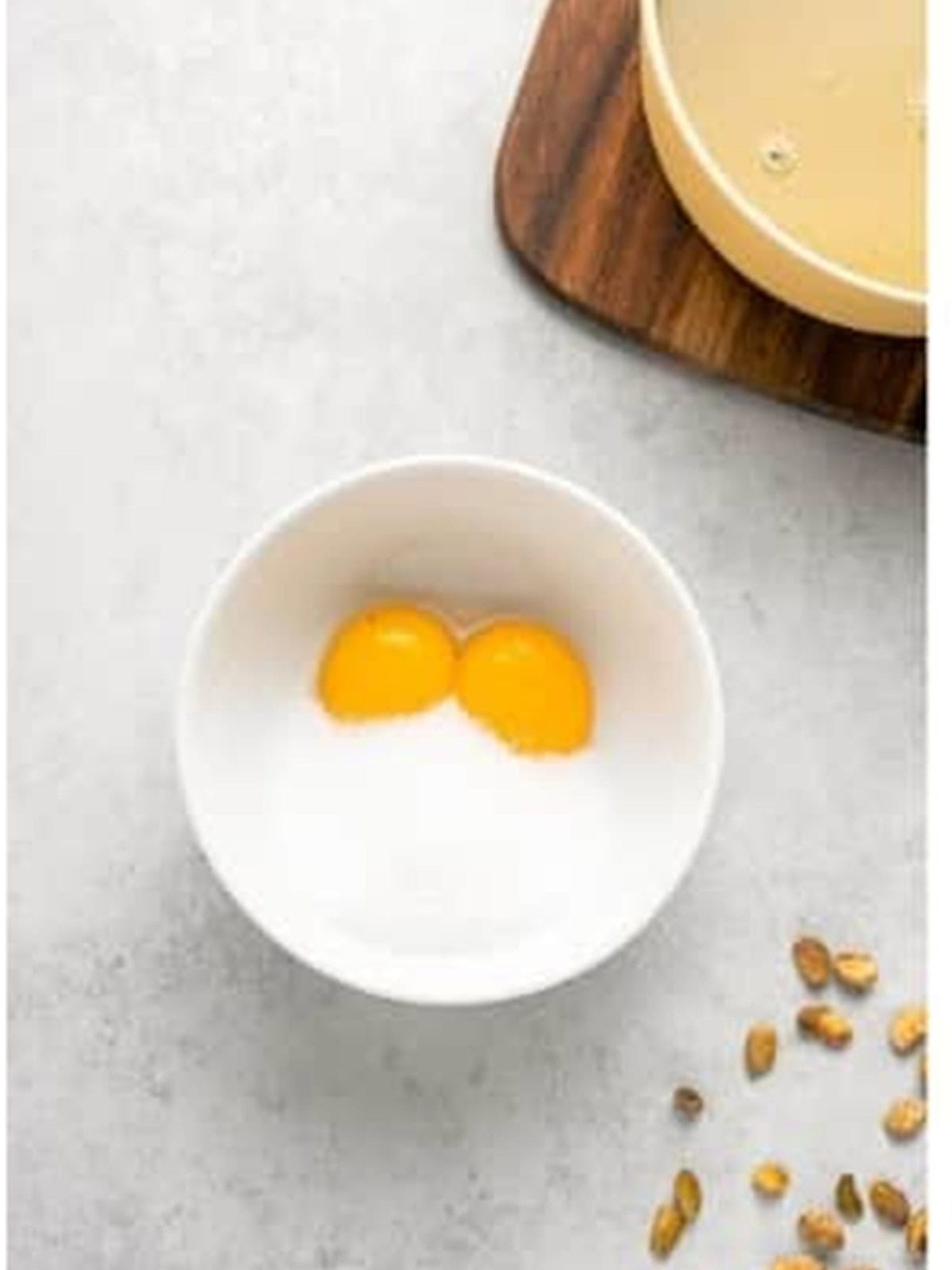Egg yolks and sugar whisked together in a white bowl for pistachio pudding recipe.