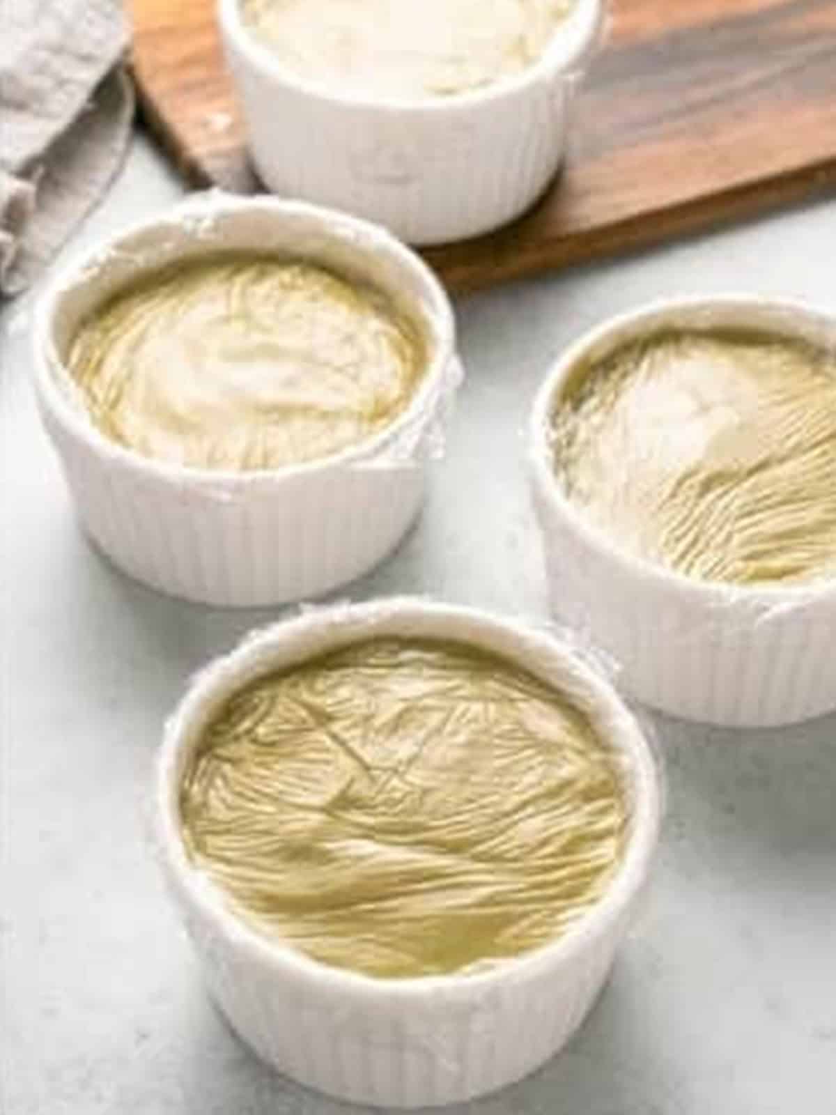 Ramekins of pistachio pudding covered with plastic wrap before chilling.