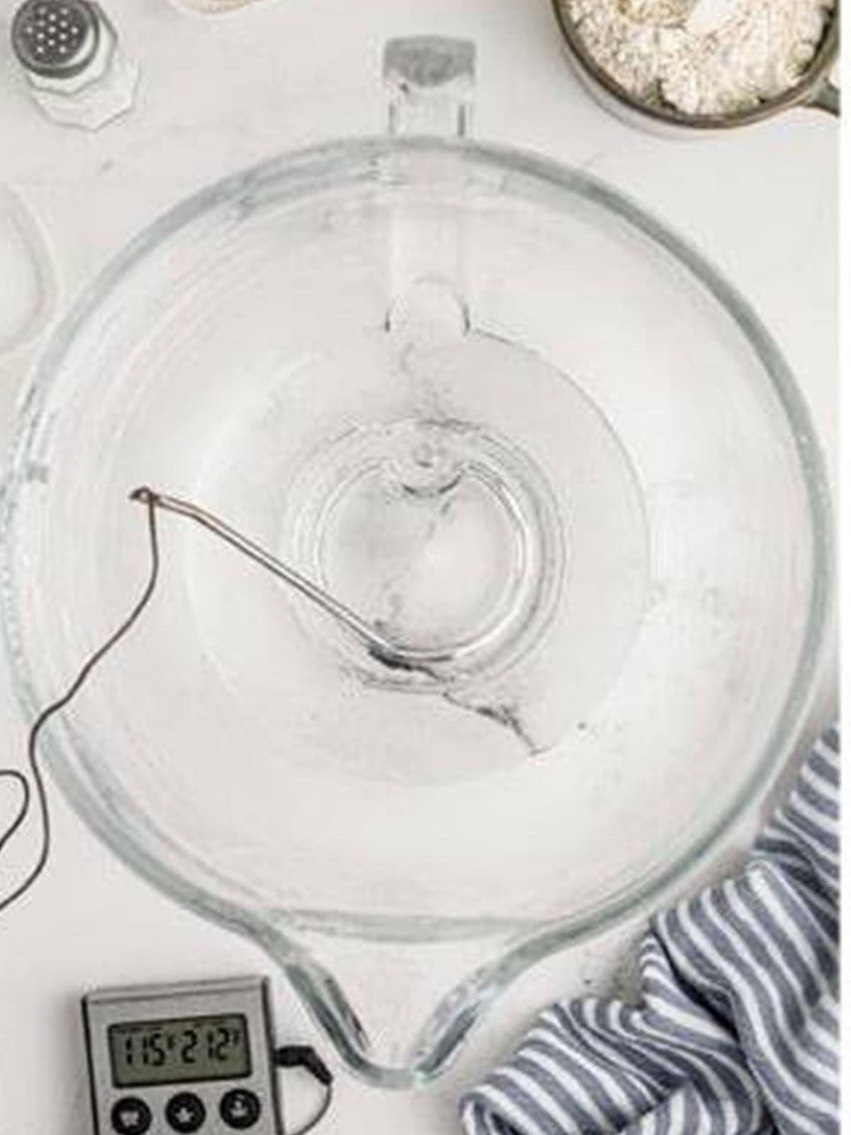 Warm water in a stand mixer bowl with a thermometer for making pizza dough.