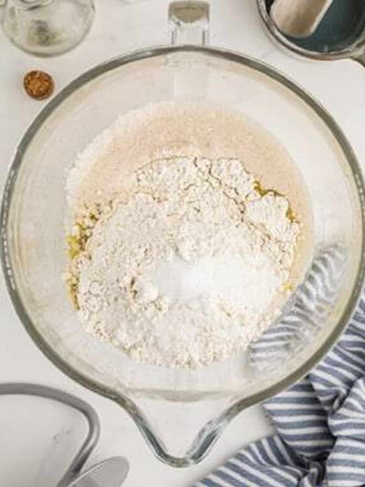 Bread flour and salt added to the bloomed yeast mixture in a stand mixer bowl.