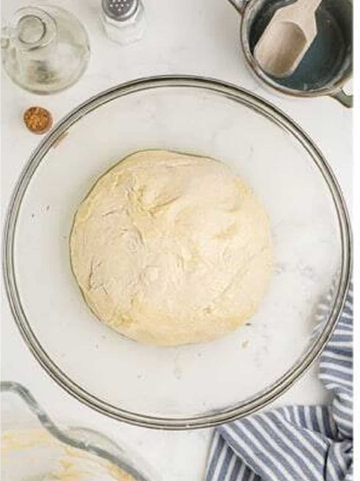 Smooth pizza dough ball mixed in a glass stand mixer bowl.
