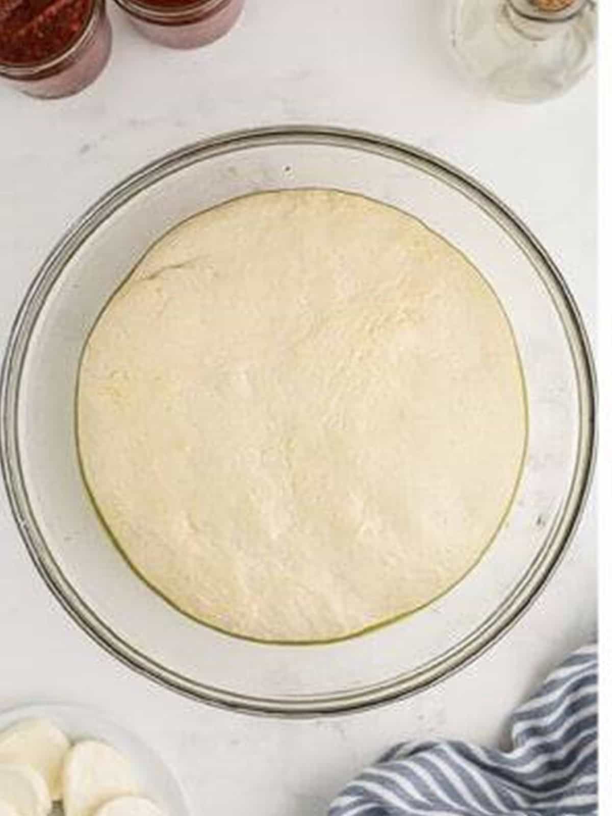 Pizza dough risen and doubled in size in an oiled bowl.
