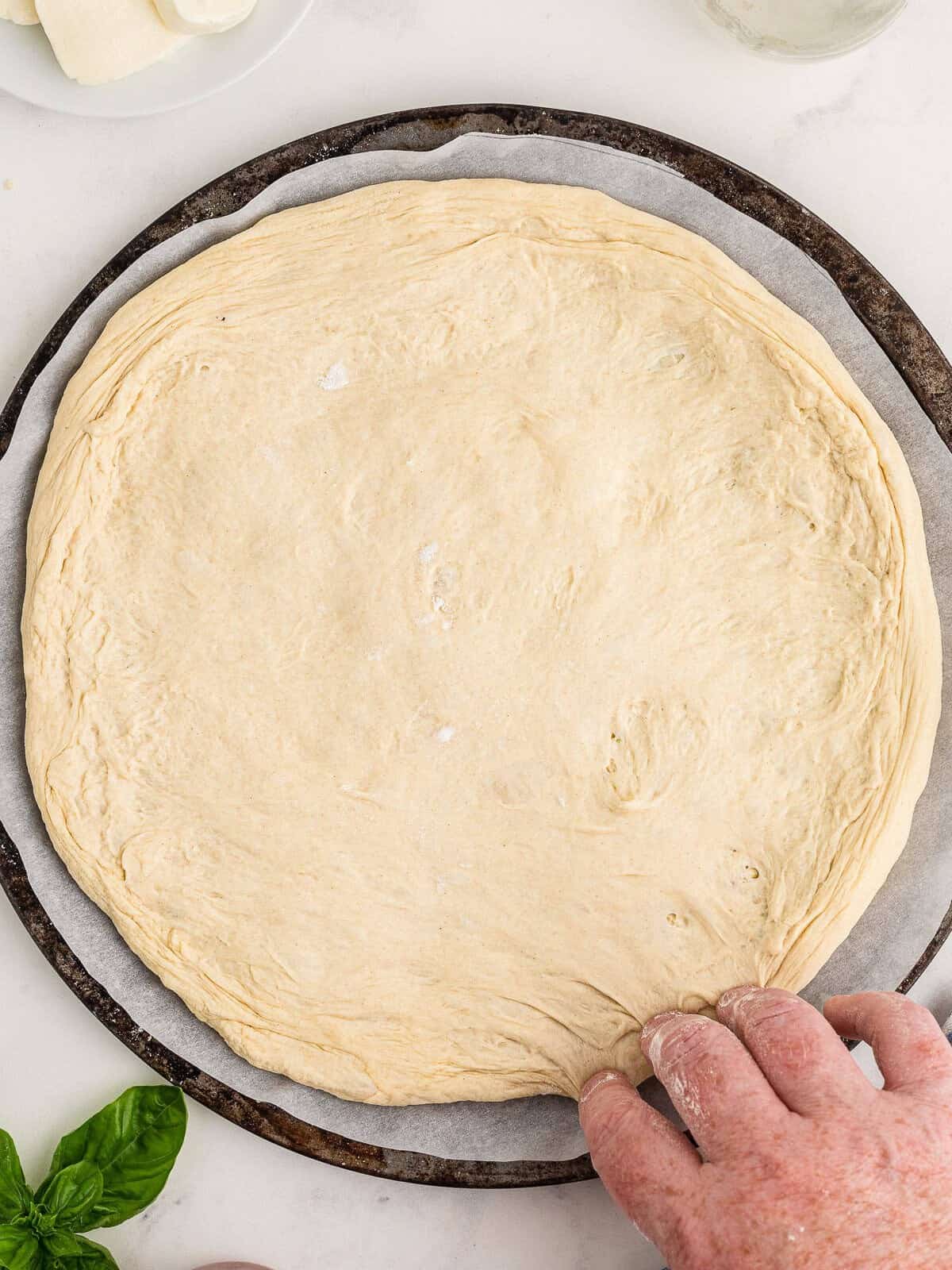 Risen pizza dough stretched into a round on a floured pizza pan ready for toppings.