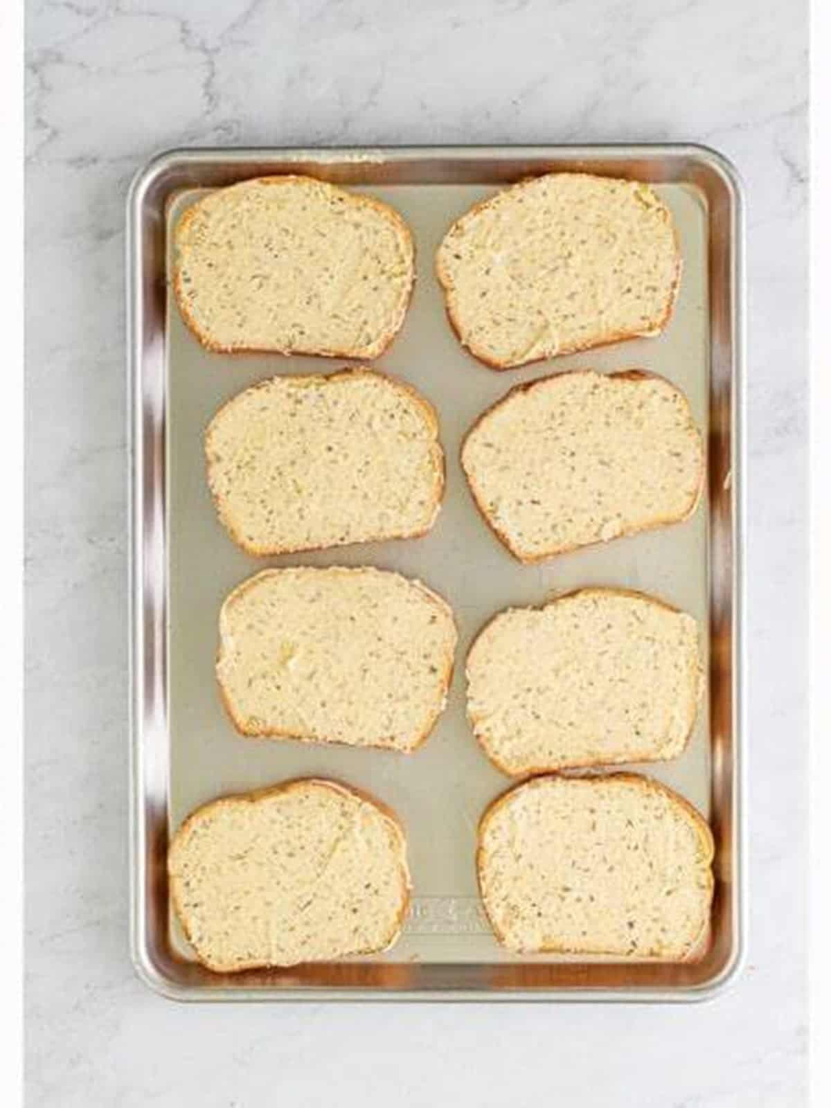 Buttered bread slices on a tray for Pizza Sandwiches.