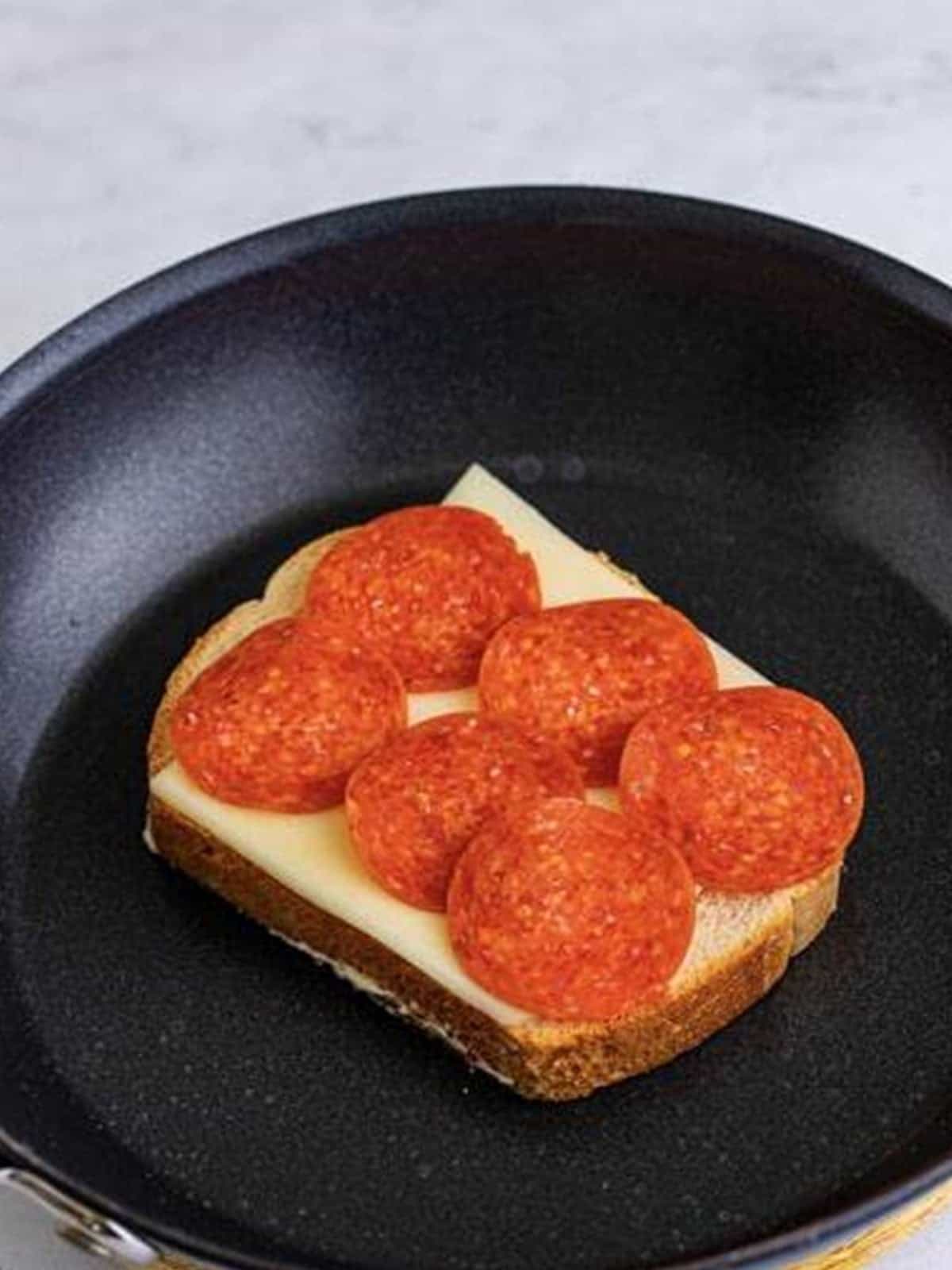 Layering mozzarella and pepperoni on bread in a skillet for a Pizza Sandwich.