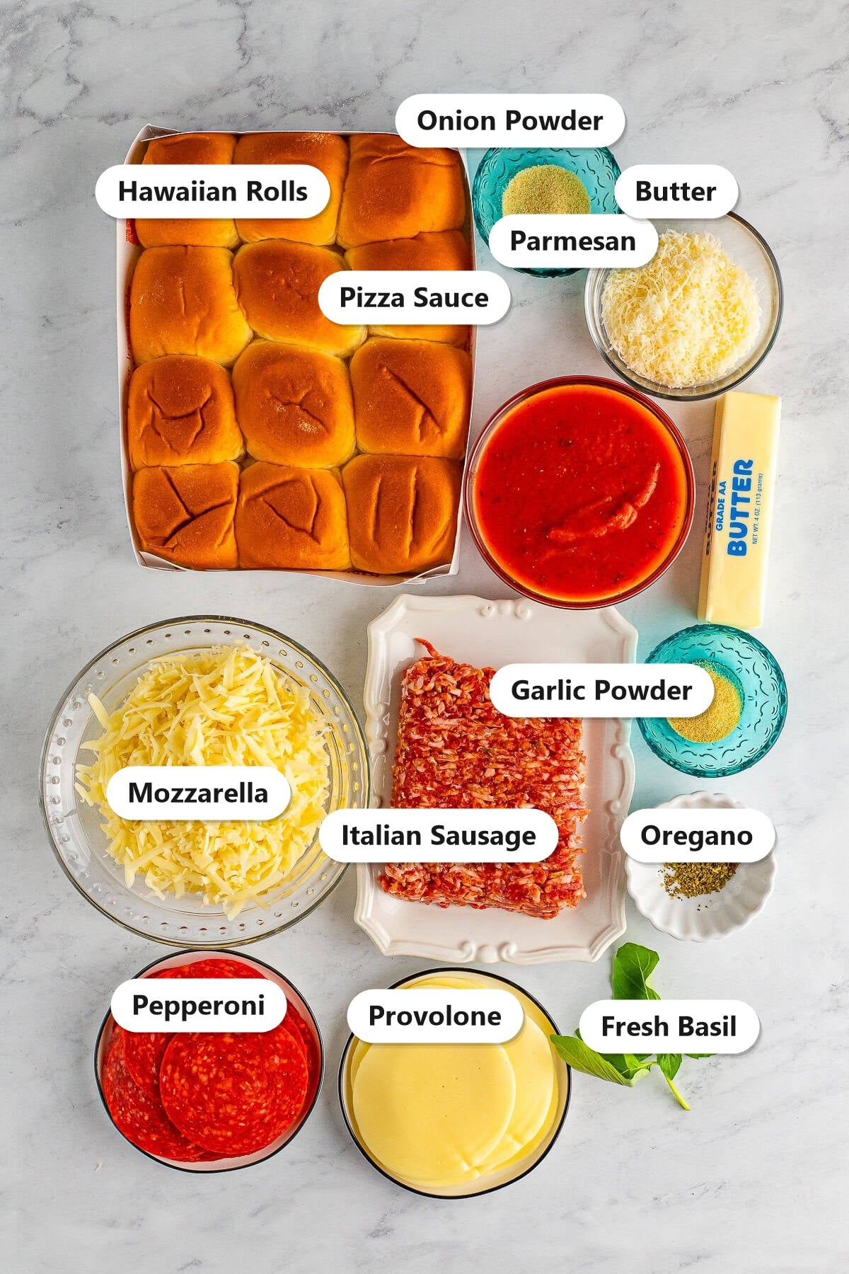 Ingredients to make pizza sliders labeled including Hawaiian rolls, Italian sausage, pizza sauce, pepperoni, mozzarella, provolone, parmesan, butter, basil, and seasonings.