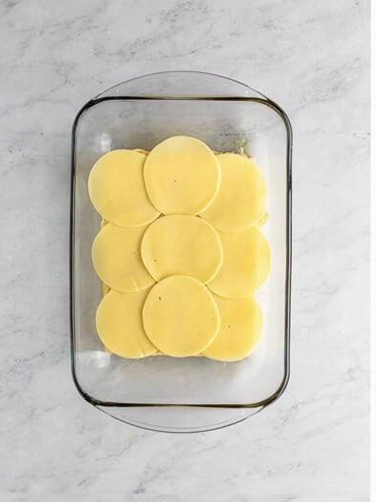 Sliced provolone layered over the bottom of Hawaiian rolls in a baking dish.