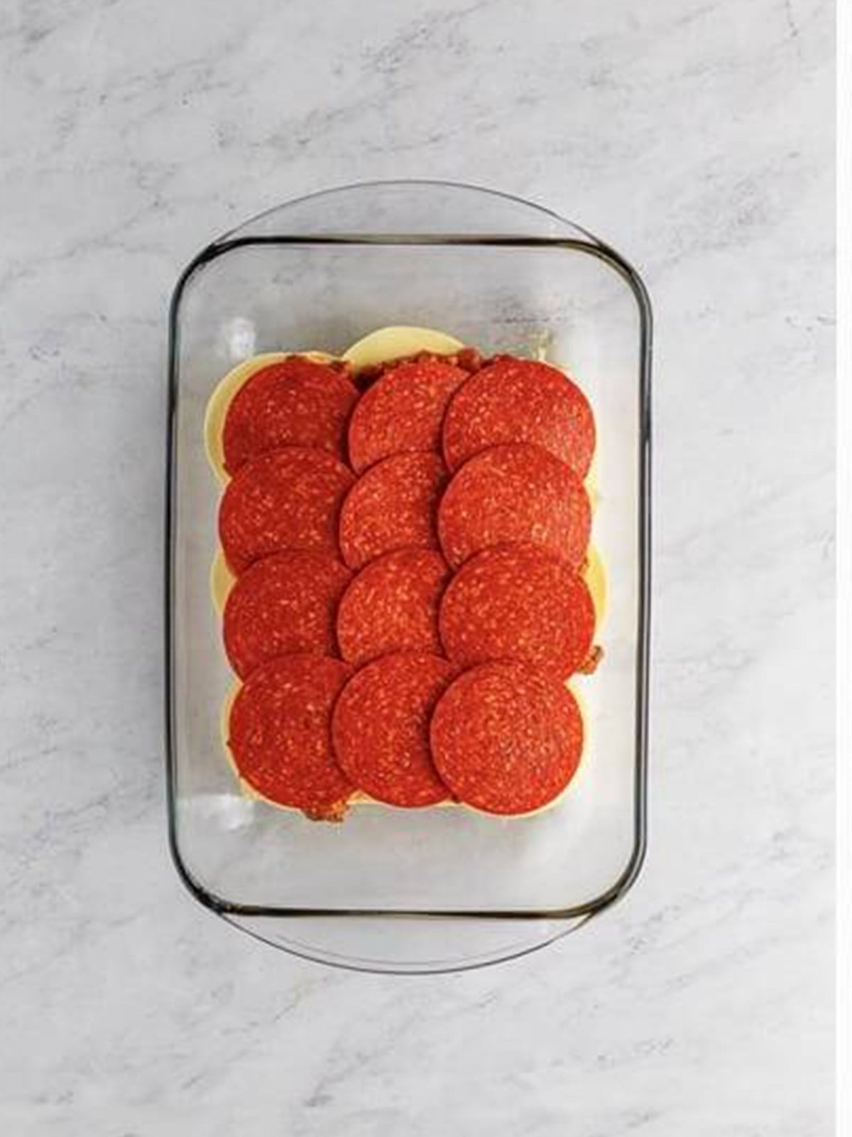 Pepperoni layered over the pizza sauce on the slider rolls.