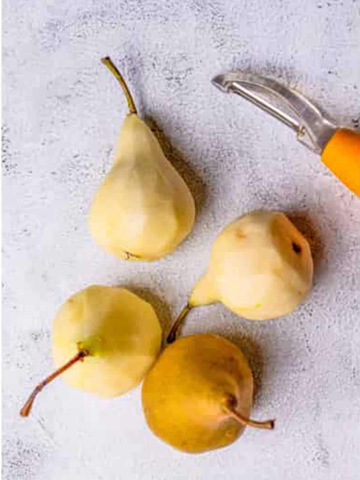 Bosc pears being peeled with the stems left on for poaching.
