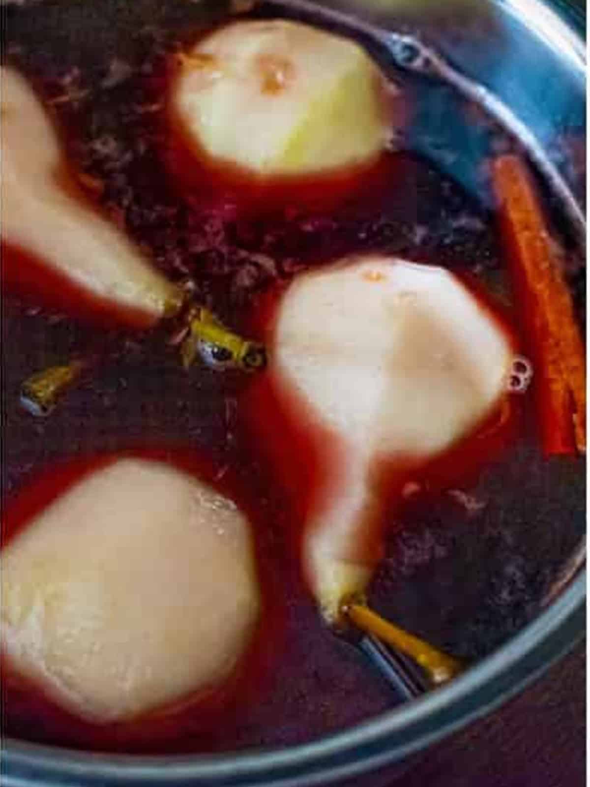 Whole pears poaching in red wine until tender and ruby red.
