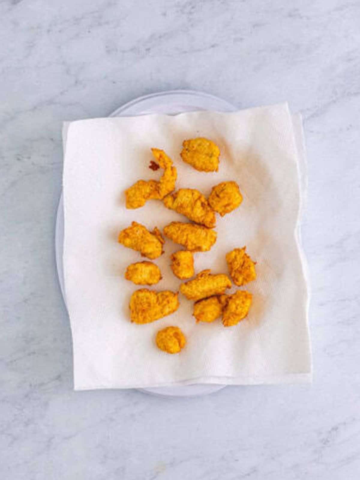Fried popcorn chicken draining on a paper towel after frying.