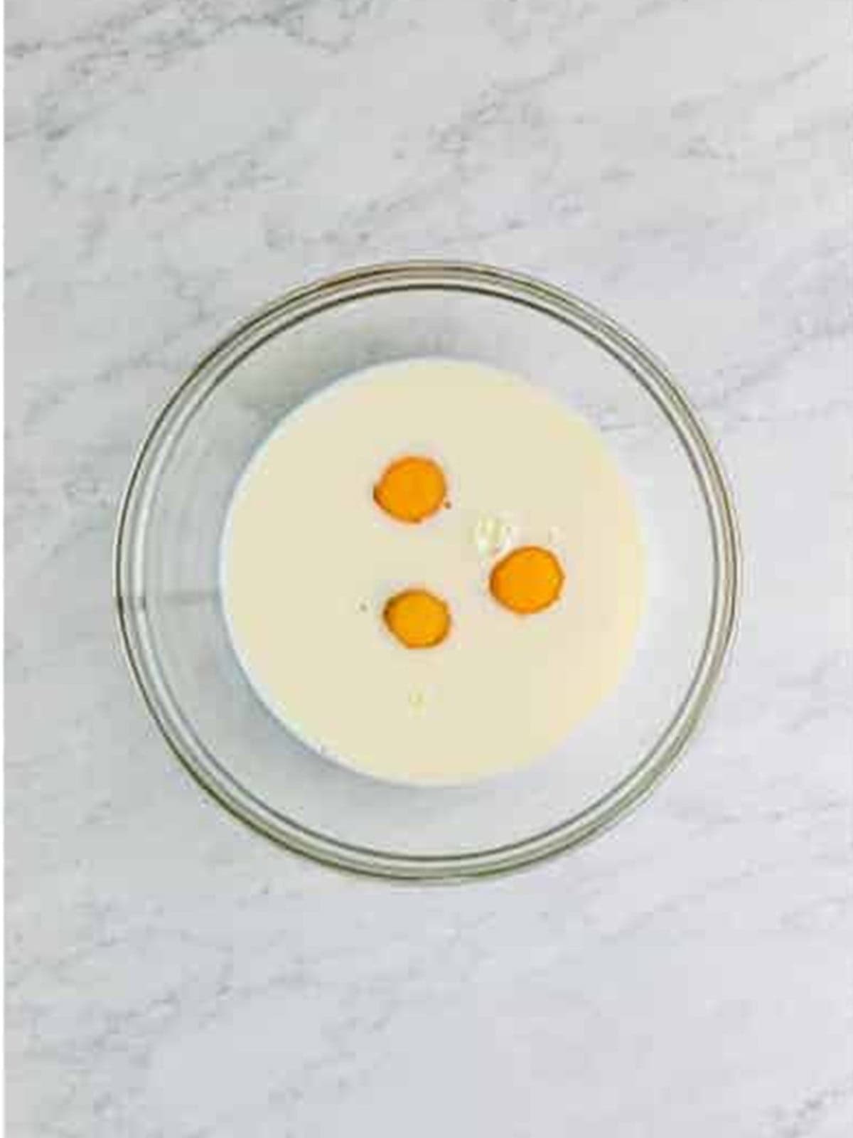 Three eggs cracked into a glass bowl for popover batter.
