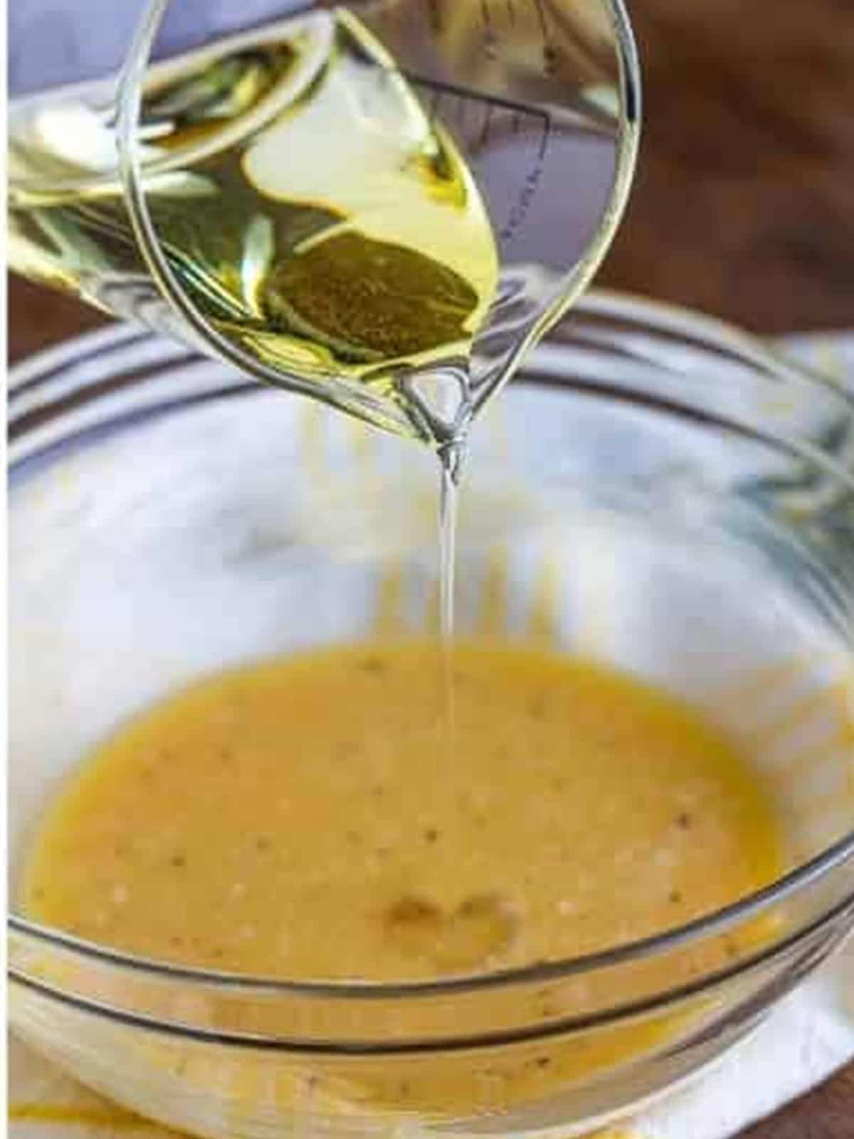 Vegetable oil being streamed into the dressing while whisking to emulsify.