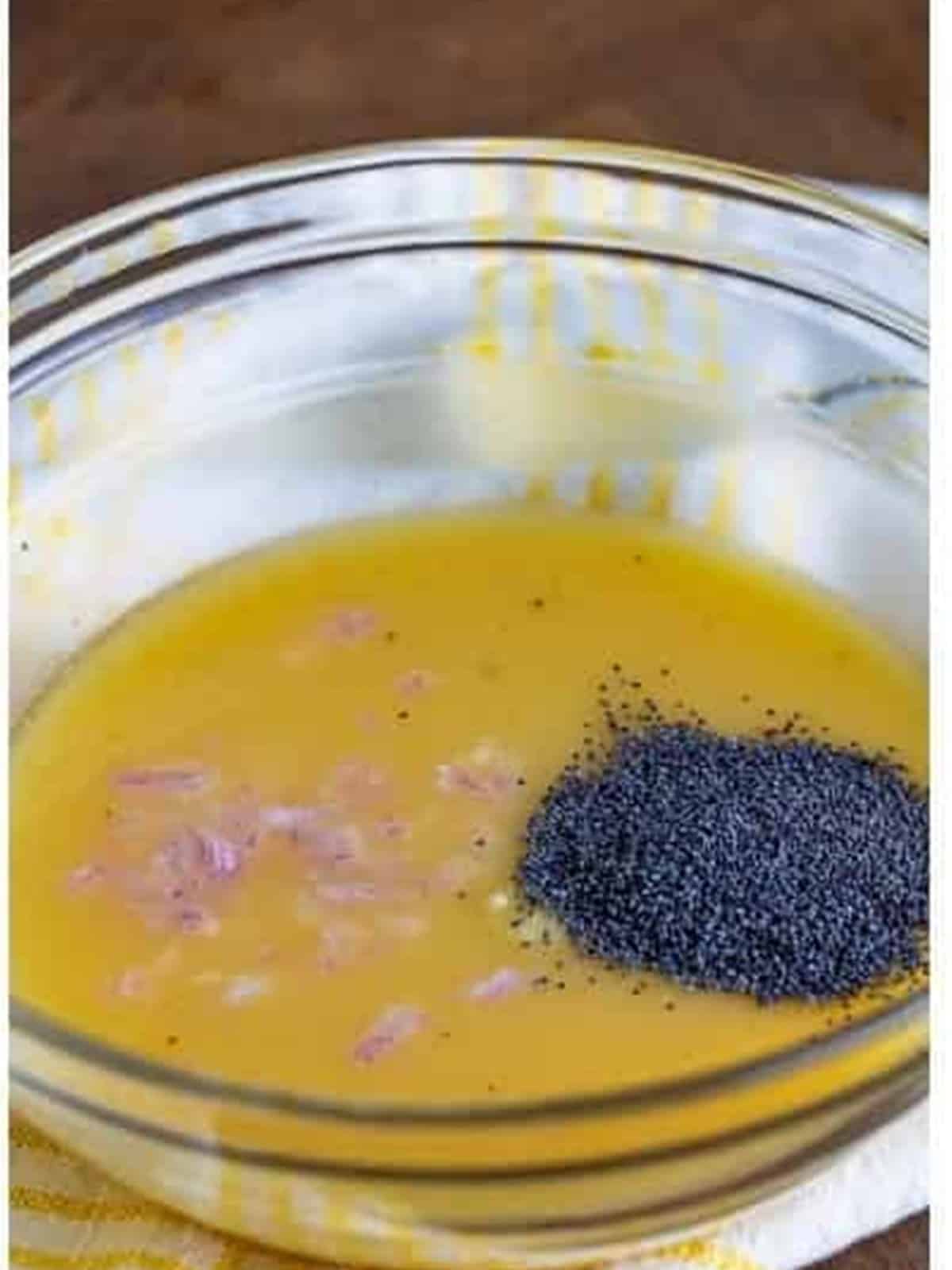 Minced shallot, poppy seeds, and garlic added to the bowl of dressing.
