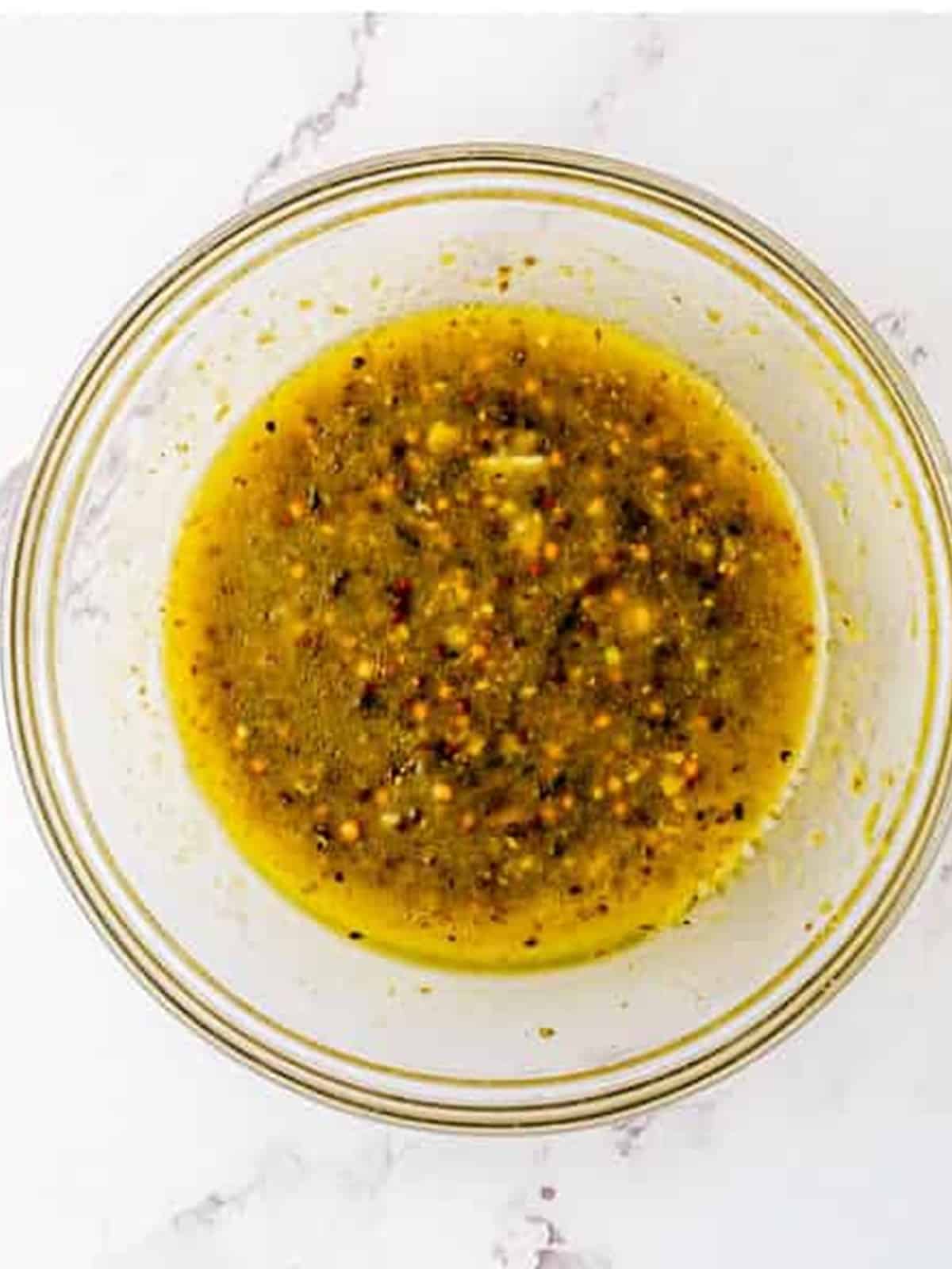 Pork chop marinade with pesto, oil, mustard, and garlic whisked together in a glass bowl.