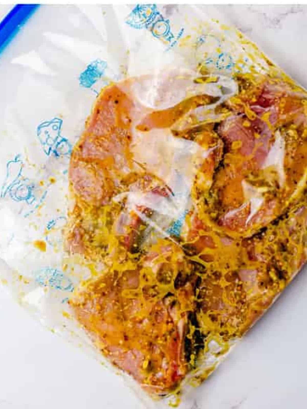 Bone in pork chops coated in marinade inside a zip top bag.