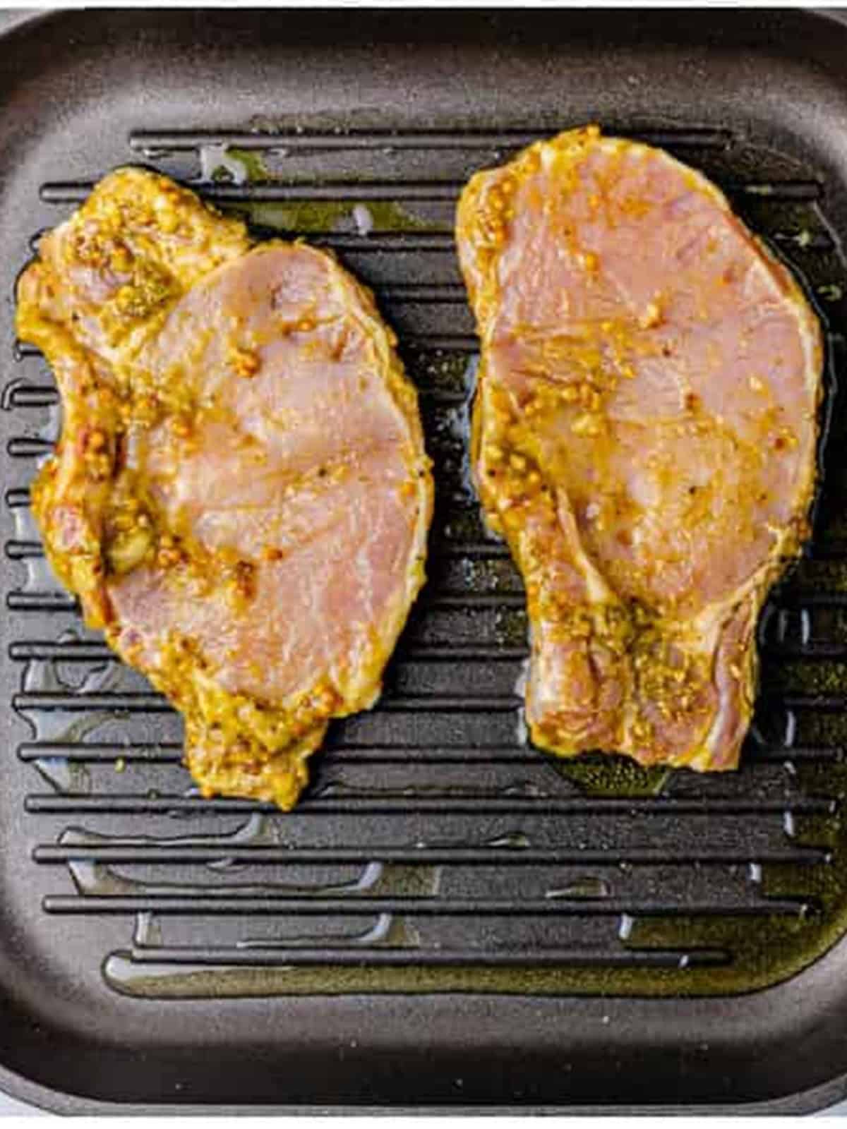 Marinated pork chops placed on a hot grill pan.