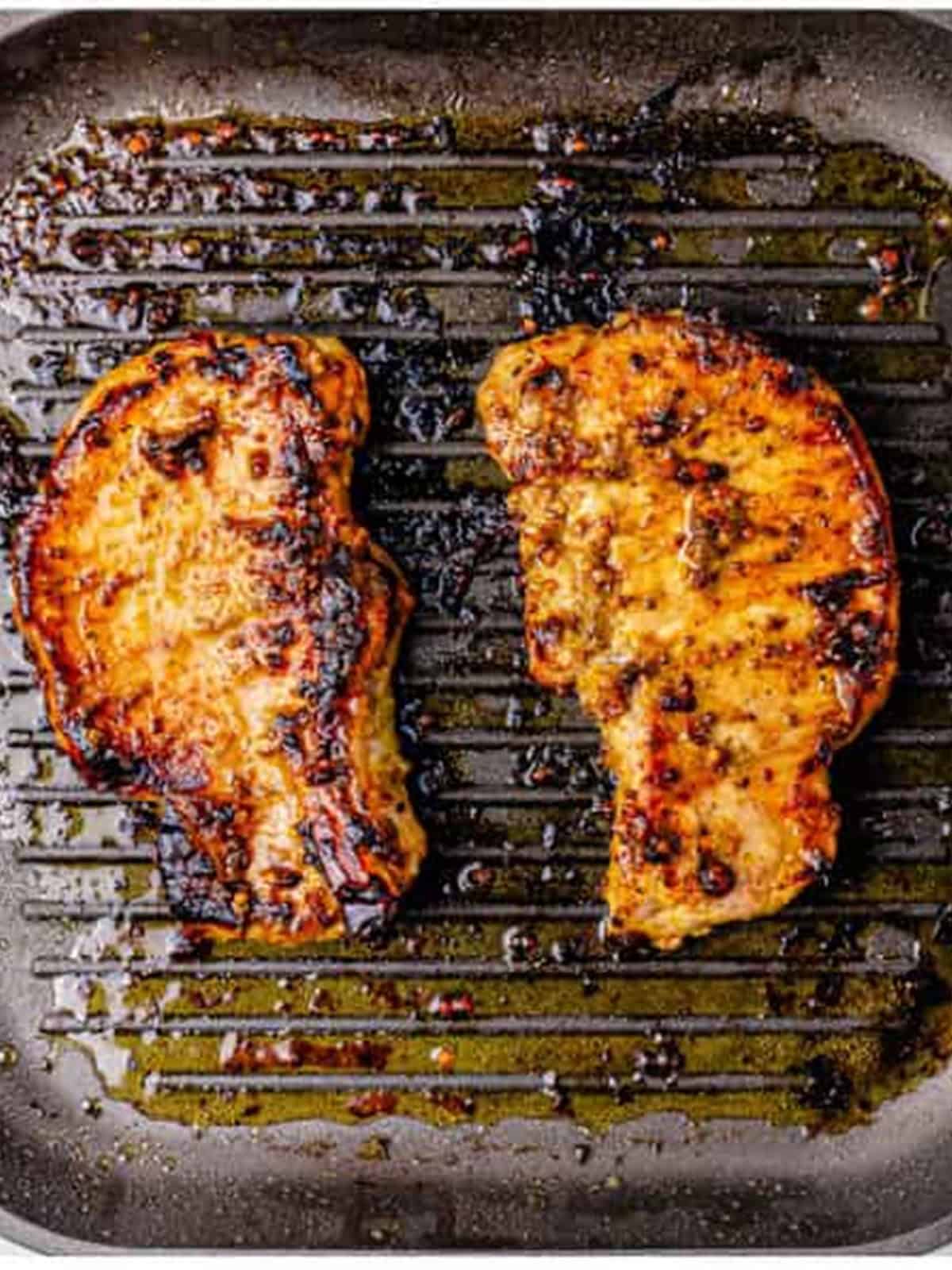 Grilled marinated pork chops with golden char marks on a grill pan.