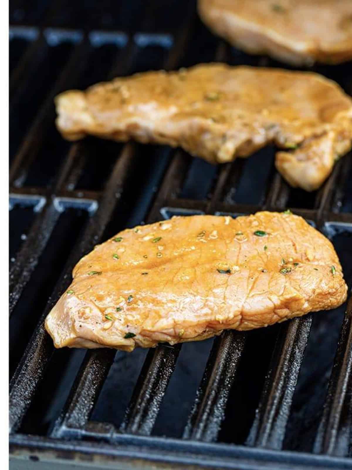 Marinated pork chops grilling with golden grill marks.