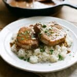 Pork chops smothered in rich brown gravy served over white rice on a plate.