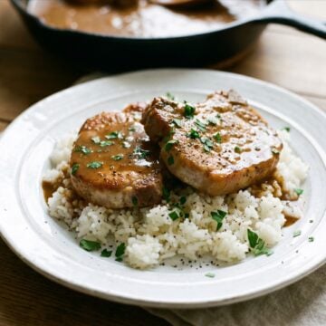 Pork chops smothered in rich brown gravy served over white rice on a plate.