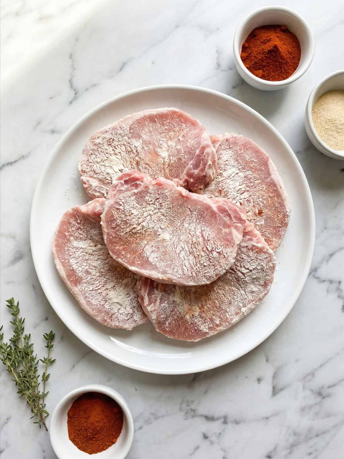 Pork loin chops coated in seasoned flour with paprika on a plate.