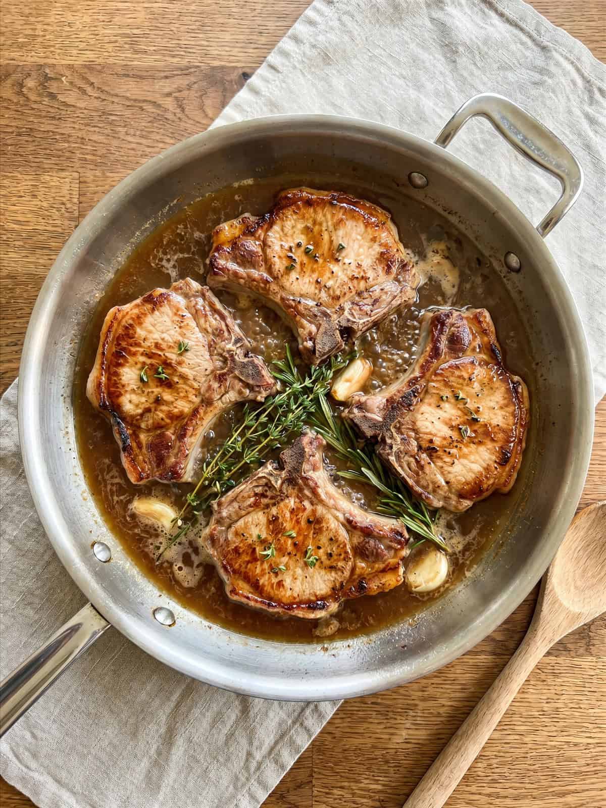 Browned pork chops simmering in beef stock in a skillet.