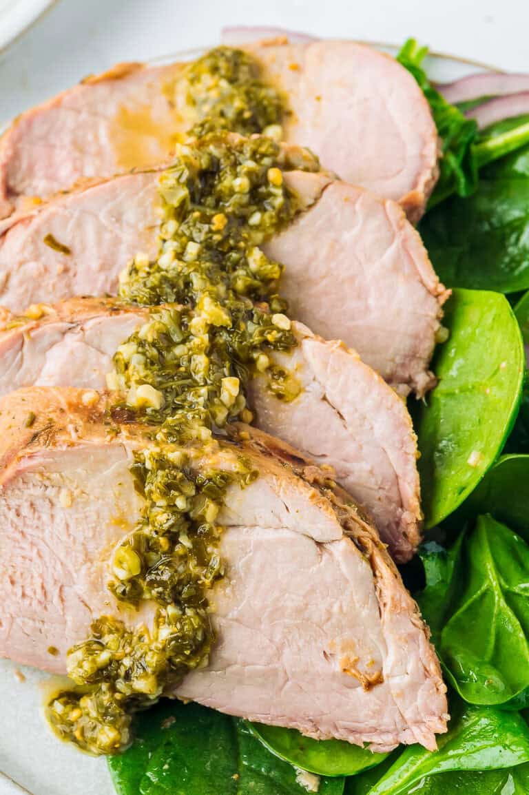 Sliced brown sugar balsamic pork tenderloin drizzled with marinade sauce on fresh greens.